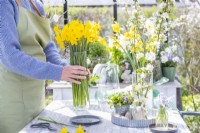 Woman placing glass vase of daffodils on table