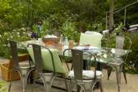 A glass dining table and metal chairs surrounded by colourful borders in Cavernona on My Mind, a sanctuary garden designed by Taina Suonio and Anne Hamiltion at the RHS Chelsea Flower Show 2023.