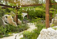 Concrete panels and a metal grid frame a pathway through perennials in the Samaritans' Listening Garden a Show Garden designed by Darren Hawkes at the RHS Chelsea Flower Show 2023