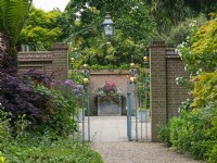 Entrance Court at East Ruston Old Vicarage Gardens, Norfolk, decorative iron work gateway, walls and containers at the beginning of Summer June