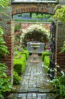 View through wrought iron gate into sunken rose garden, with distant bench under rose arbor and planted urn as focal point - Open Gardens Day, Waldringfield, Suffolk