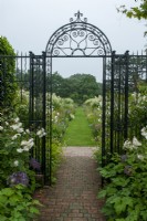 Decorative wrought iron entrance gate to classical 16th century garden, with view to grass path and deep herbaceous borders on either side  - The Walled Garden, Helmingham Hall, Suffolk