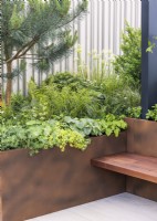 Corner of a rooftop garden with plant container and integral bench, summer June