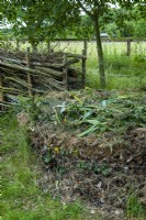 Circular compost heap within wire netting surround and dead boughs stacked between poles beyond - Open Gardens Day, Easton, Suffolk