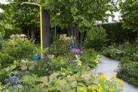 A stone path winds deeper into a therapeutic green space, passing between borders of herbaceous perennials, into the shade of Parrotia persica and to colourful, sheltered seating areas.
