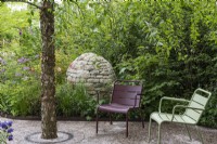 A tranquil shady seating area beneath Betula nigra, overlooked by a stone cairn immersed in a border with roses and thalictrum.