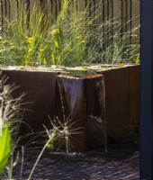 Rusted metal raised water feature with water falling into pond beneath metal grill - Fenton Gardens Ltd SubAqua - BBC Gardeners' World Live 2023, Birmingham NEC - Designer Joshua Fenton