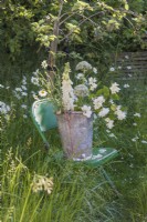 Bouquet of white flowers in metal bucket on green metal chair in meadow - Alliums, Leucanthemum vulgare, Philadelphus, Nigella and Digitalis purpurea