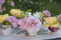 Pink and yellow roses displayed in vintage china teacups on painted tray