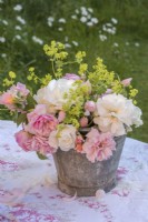 Pink and yellow roses displayed in metal bucket on patterned tablecloth