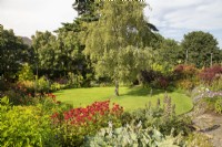 North House Garden featuring perennial borders surrounding a circular lawn; Monarda 'Gardenview Scarlet' in foreground