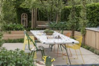 A community garden enclosed in hornbeam hedges, separated by raised beds of vegetables into a dining area, and a quiet space with swingseat shaded by trees.