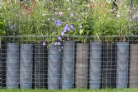 A low boundary is created from metal gabions filled with plastic plant pots, a clever way of upcycling waste plastic. The topmost pots are planted with grasses and flowering perennials.