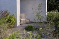 A seat rests in a pavilion, overlooking a tranquil garden planted with trees, shrubs and grasses.