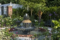 A formal courtyard garden inspired by Charleston, South Carolina, has a central pineapple shaped fountain, surrounded in beds of palms and exotics combined with shrub roses, hydrangeas and perennials. Paths are laid with crushed shells.
