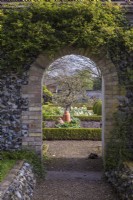View through archway in flint wall into spring walled vegetable garden