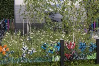 A playful way of upcycling waste plastic bags by weaving them into the chickenwire fence. Behind, a birch grove and meadow of wildflowers and grasses.