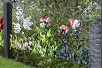 A playful way of upcycling waste plastic bags by weaving them into the chickenwire fence. Behind, a meadow of wildflowers and grasses. 