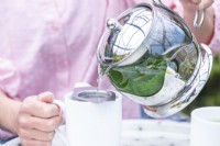 Woman pouring nettle tea through a strainer into mugs