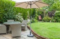 Rattan table and chairs on dining area of patio with sunshade, nearby Rosa 'Bonica 82' and sweeping border of contrasting shrubs and perennials