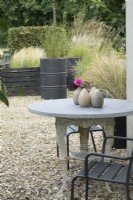 Gravel terrace. Classic iron table leg with marble top and old black painted barrels planted with several grasses. Dahlia in ceramic vase.