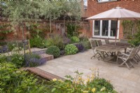 Walled courtyard garden with garden furniture, sandstone paving, dry borders and pleached Pyrus salicifolia 'Pendula' and pool