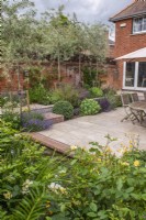 Walled courtyard garden with sandstone paving, dry borders and pleached Pyrus salicifolia 'Pendula' and small brick edged pool