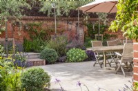 Walled courtyard garden with garden furniture, sandstone paving, dry borders and pleached Pyrus salicifolia 'Pendula' 