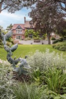 View across lawn to house with water feature and terrace from pastel border with wild duck sculpture
