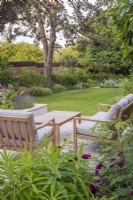 View across seating area on terrace to lawn, trees and borders with brick and willow boundaries