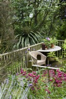 Terrace with wooden balustrade, table and seat surrounded by lush foliage in a July garden