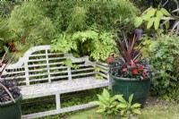 Glazed green container planted with cordyline and dahlias beside a Lutyens bench in a July garden.