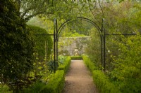A pathway under a metal arch bordered  by Taxus baccata hedge leading to a stone urn in the Crathes Castle Walled Garden.