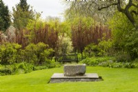 A stone trough and garden bench surrounded by lawn and trees in the Trough Garden in the Crathes Castle Walled Garden.