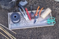 Wire, eyelet screws, ferrules, tensioners, pliers, pencil, tape measure, secateurs, string and scissors on wooden tray