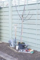 Ficus tree, watering can, digging fork, trowel, drill, bamboo canes, wire, eyelet screws, , ferrules, tensioners, pliers, pencil, tape measure, secateurs, string and scissors laid out on the ground