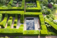 Clipped formal hedges of Taxus baccata - Yew, forming garden rooms, one containing a pool with dramatic reflections of the cloudy sky. Image taken with drone. June. Summer. 