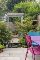 Single pergola constructed from scaffold poles and half oak sleepers in small enclosed urban garden with rectangular pool and seating
