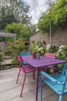 Colourful table and chairs on small paved enclosed urban garden featuring recycled scaffold pergolas and pool