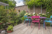 Small enclosed paved urban garden with patio and colourful furniture, scaffold pole pergolas and small rectangular pool and containers.  Plants include Hydrangea 