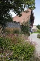 Mixed perennials dominated by Persicarias with Calamagrostis x acutiflora 'Overdam'. White gravel path. View to Library building. August