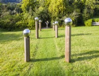 Meadow that has been cut with avenue of columns of wood capped with stainless steel globes leading to mobile sculpture by Stuart Stockwell. September. Image taken with drone. 