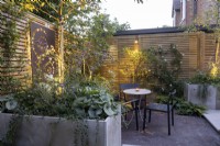 Courtyard garden at dusk with lighting, seating area, raised beds and contemporary wood boundary fence