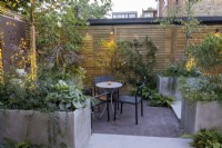 Courtyard garden at dusk with seating area, stone raised beds and contemporary wood boundary fence and lighting