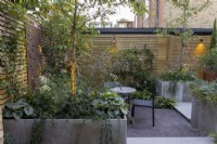 Courtyard garden at dusk with seating area with raised beds and contemporary wood boundary fence and lighting