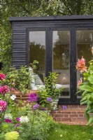 Black summerhouse with glass doors with border of Dahlias,  and annuals