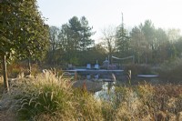 Natural swimming pool with seating area surrounded by ornamental sunlit grasses