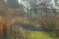 Rustic coppiced ash gazebo surrounded by ornamental grasses and perennials in winter.