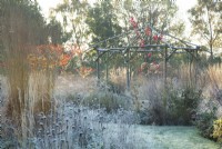 Rustic coppiced ash gazebo surrounded by ornamental grasses and perennials in frost
