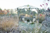 Frosted coppiced ash gazebo and seating area surrounded by ornamental grasses and perennials